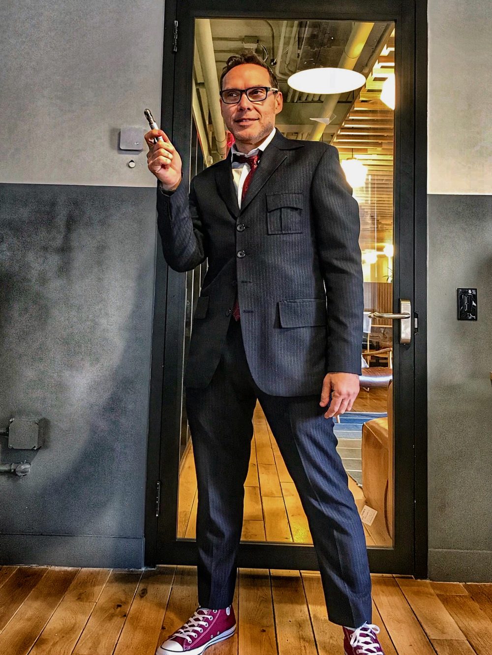 Laurence Hewitt in a pinstripe suit, bow tie and red trainers, holding a sonic screwdriver